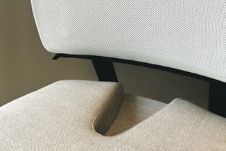 Grijze stof zitbank met zwart metalen frame tegen beige muur, detail van armsteun en zitting.