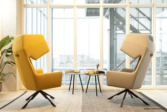 Twee design fauteuils met hoge rug en draaivoet: één geel en één beige, tegenover elkaar bij kleine tafels in lichte kantoorr