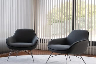 Twee grijze loungefauteuils met metalen poten in moderne kantoorruimte met raampartijen en verticale lamellen.