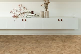 Witte lage kasten met rood-bruine handgrepen tegen witte muur. Bovenop decoratieve elementen: gedroogde bloemen, kaarsen, vaz