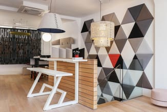 Modern kantoor met houten receptiebalie, witte designstoelen, geometrische akoestische wandpanelen in grijs/zwart/rood, hange