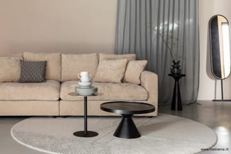 Beige modulaire loungeset met zwarte bijzettafels, ronde vloerkleed, grijze gordijnen, zwarte staande spiegel en zwarte plant