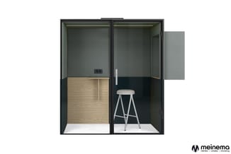 Twee zwarte akoestische belcellen naast elkaar, links met houten wand, rechts met barstoel, beide met grijze bovenwanden en g