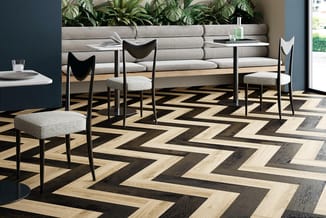 Moderne lounge-inrichting met grijze zitbank, zwarte stoelen met grijze zittingen, metalen tafel en geometrisch houten vloerp