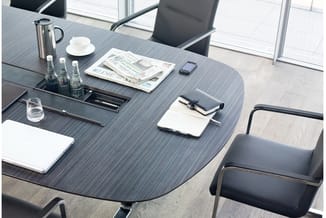 Moderne vergadertafel met grijze houten blad, zwarte stoelen, laptops, notitieblokken, waterflessen en koffiekan in lichte ka