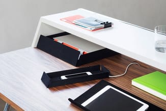 Wit bureau met zwarte kabelorganizers, notitieblokken en tablet op houten werkblad, glas water rechtsboven.