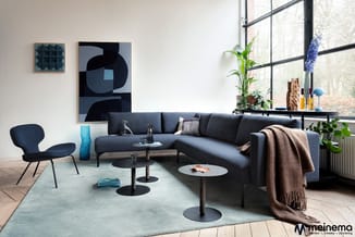 Moderne woonkamer met donkergrijze hoekbank, blauwe fauteuil, zwarte bijzettafels en mint groen tapijt bij groot raamfront.