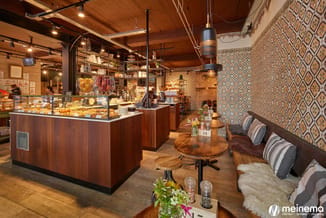 Modern koffiebar met houten theken, bruine houten tafels, grijze gestoffeerde banken, geometrisch behang en houten plafond me