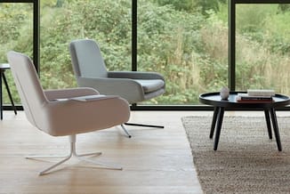 Twee grijze design fauteuils met chromen pootjes en zwarte salontafel in moderne kantoorruimte met grote ramen en groen uitzi