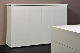 Witte kastenwand met vier deuren en metallic bovenrail in modern kantoorinterieur met donkere vloer.