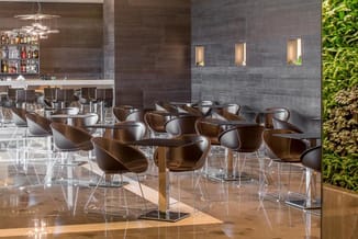Modern hospitality space met bruine leren stoelen op chromen poten, houten tafels, bar met glazen rekken, grijze tegelwanden