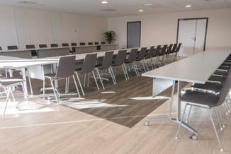 Moderne vergaderruimte met lange witte tafel, zwarte stoelen met metalen onderstel, houten vloer en witte wanden met grijze d