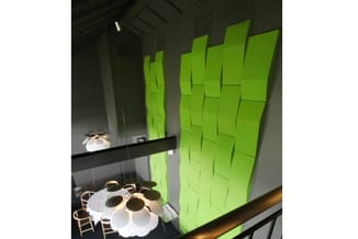 Groene akoestische wandpanelen in moderne kantoorruimte met ronde witte tafel, houten stoelen en hangende verlichting.