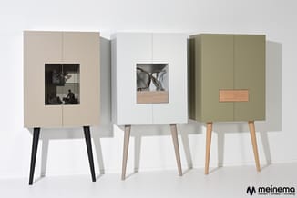 Drie moderne kasten met glazen vitrineopening en houten accent, in beige, wit en olijfgroen, op schuine poten.