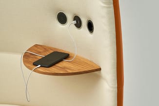 Hoekplank in hout aan beige stofwand bevestigd, met smartphone en witte oplaadkabel. Drie ronde luidsprekers boven geplaatst.