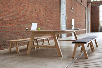 Houten vergadertafel en bijpassende banken in minimalistisch design tegen bakstenen muur in industrieel kantoor.