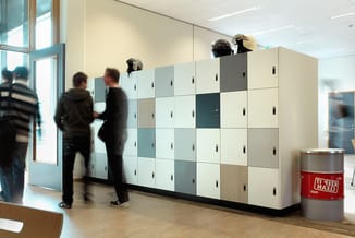 Modulaire kastenwand in kantoor met lichte kleuren en houtaccenten, helmen bovenop, personen in beweging.