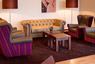 Loungeruimte met gele Chesterfield-bank, paarse en rode gestreepte fauteuils, houten salontafels, bruine vloerbedekking en wa
