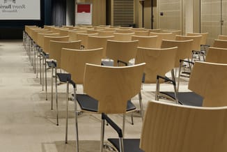 Vergaderruimte met rijen houten stoelen met zwarte zitting en metalen frame, gericht op een presentatiescherm aan de achterwa