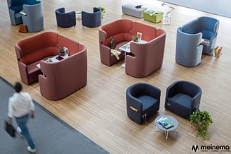 Moderne kantoorcollectie met ronde fauteuils in rood, blauw en grijs op houten vloer, enkele met tafeltje en plantenbak erbij