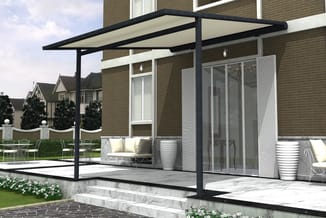 Zwarte pergola met beige schaduwdoek boven terras met grijze loungebank en witte poefs naast bakstenen woning.