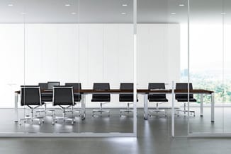 Modern kantoor met lange houten vergadertafel, zwarte bureaukstoelen, witte kolommen en grote ramen met uitzicht.
