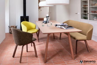Vergadertafel met houten onderstel en lichte blad, omgeven door drie moderne stoelen in geel, grijs en zand, op terracotta te