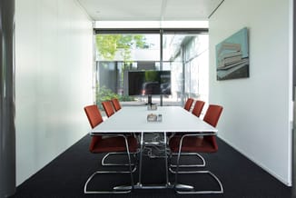 Moderne vergaderruimte met witte wanden, zwarte vloer, rechthoekige witte vergadertafel en zes rode gestoffeerde stoelen met