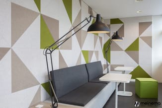 Kantoorruimte met grijze loungebank, witte tafels, zwarte bureaulampen en driehoekig gemotiveerde wandbekleding in groen, bei