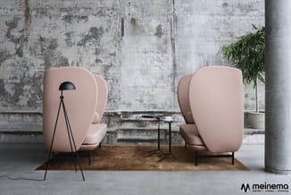 Twee roze gestoffeerde fauteuils met hoge rug, zwarte statief lamp, klein zwart tafeltje, op houten mat tegen gestructureerde