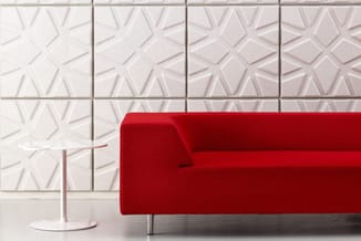 Rode moderne bank met metalen poten tegen witte tegelmuur met geometrisch patroon, naast wit bijzettafeltje.