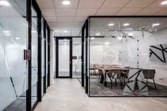 Kantoorgang met zwarte glazen afscheidingen, witte frosted glass deuren, grijze vloer en moderne plafondverlichting. Zicht op