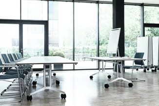 Moderne vergaderruimte met twee witte vergadertafels op wielen, zwarte stoelen, grote glazen wanden en uitzicht op groen land