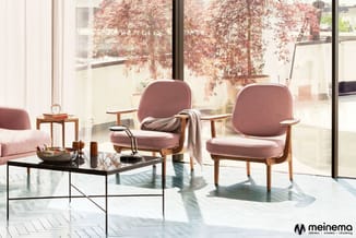 Moderne lounge met twee roze stoelen en zwarte tafel bij grote ramen met uitzicht op terras met rode klimplanten.