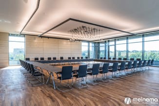Moderne vergaderzaal met lange houten tafel, zwarte kantelstoelen, houten vloer, betonnen wanden en glazen wanden met uitzich