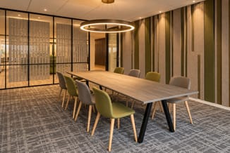 Rechthoekige Halden Verde vergadertafel met houtkleurig blad en zwarte poten, omringd door groene en grijze stoelen.