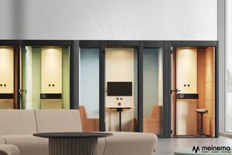 Moderne kantoorruimte met grijze zitbank, zwarte ronde salontafel en drie besprekingscellen met gekleurde interieurafwerkinge