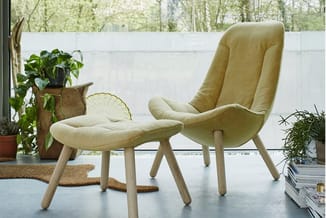 Geel-groen fauteuil met houten poten en bijpassende voetsteun in moderne kantoorruimte met planten en raam.