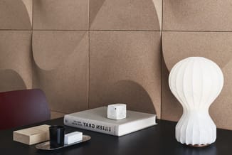 Moderne werkplek met beige geluidsabsorberend wandpaneel, zwart bureau, witte bolvormige lamp, boek "Helen Gray You Work Here