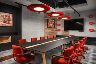 Moderne vergaderruimte met lange zwarte tafel, rode ergonomische stoelen, rode hangende cirkellampen en Coca-Cola branding op