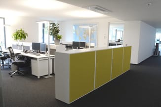 Modern kantoor met geel-groene akoestische scheidingswanden, witte werkplek met monitors, zwarte bureaustoel en groene plante