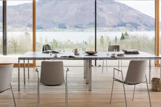 Vergadertafel met grijze stoelen in moderne kantoorruimte met glazen wand en uitzicht op meer en bergen.