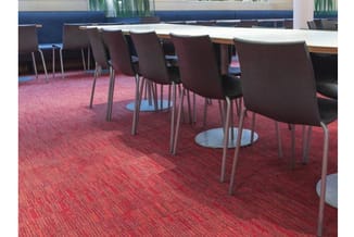 Bruine kantoorstoel met metalen poten in vergaderruimte op rood tapijt, meerdere stoelen langs tafel.