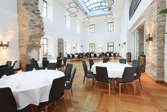 Moderne vergaderruimte met ronde tafels, witte tafelkleden, zwarte stoelen met houten poten, stenen kolommen, houten vloer en