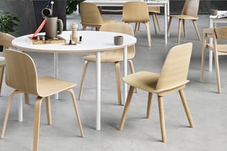 Ronde witte eettafel met houten stoelen in naturel hout en wit onderstel, geplaatst in moderne kantoorruimte met betonvloer.