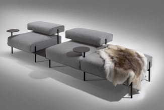 Modulaire grijze loungebanken met zwarte metalen poten en bijzettafels, hond loopt erlangs.