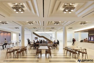 Moderne kantoorruimte met houten eettafels en stoelen, plafond met inbouwspots, witte wanden, kolommen en trap. Meinema-logo