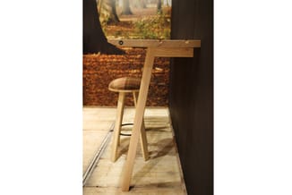 Houten barkruk met geruit zitting en voetsteun in lichte houten afwerking, geplaatst aan een bartafel in een kantooromgeving.