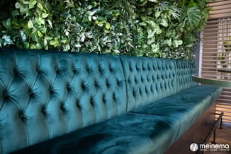 Turquoise chesterfield bank met gestoffeerde rugleuning tegen groene plantenwand in modern kantoor.