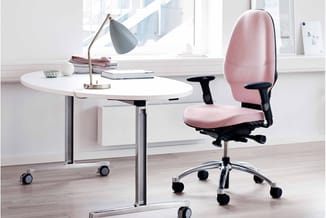 Moderne kantoorwerkplek met ronde witte tafel, grijze bureaulamp, roze ergonomische bureaustoel en grote ramen met uitzicht.